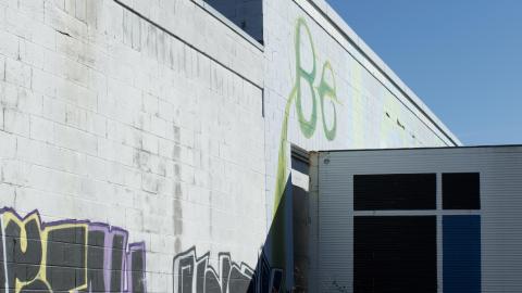 Back of the building, with trailer stopping adjacent to the graffiti. It casts a shadow across the half of the nearest words.